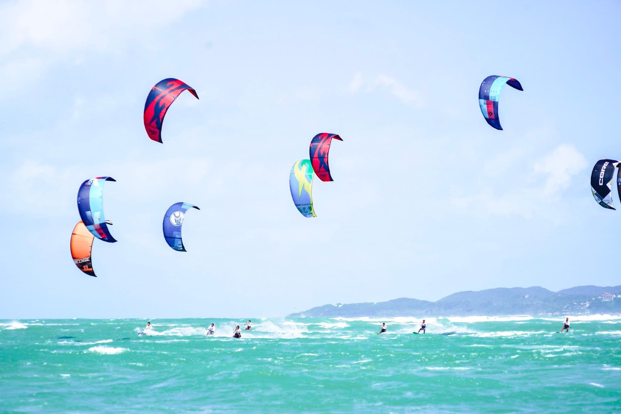 Grupo de kitesurfistas com pipas coloridas no céu sobre o mar verde de Pipa