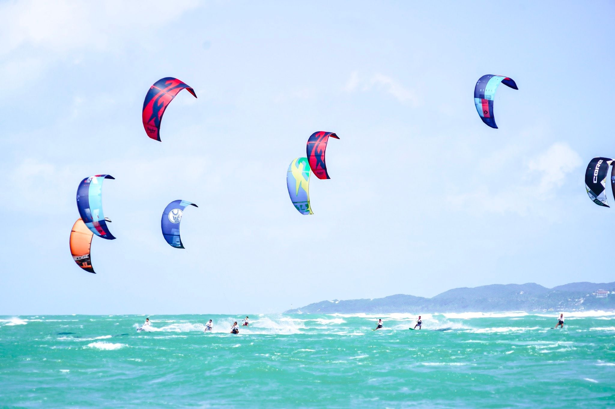Grupo de kitesurfistas com pipas coloridas no céu sobre o mar verde de Pipa