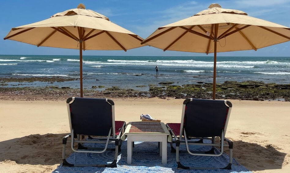 Duas cadeiras de praia com guarda-sol em frente ao mar de Sibauma com pedras visíveis