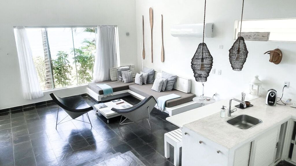 Sala de estar moderna branca com luminárias de arame preto, sofá cinza e cozinha americana