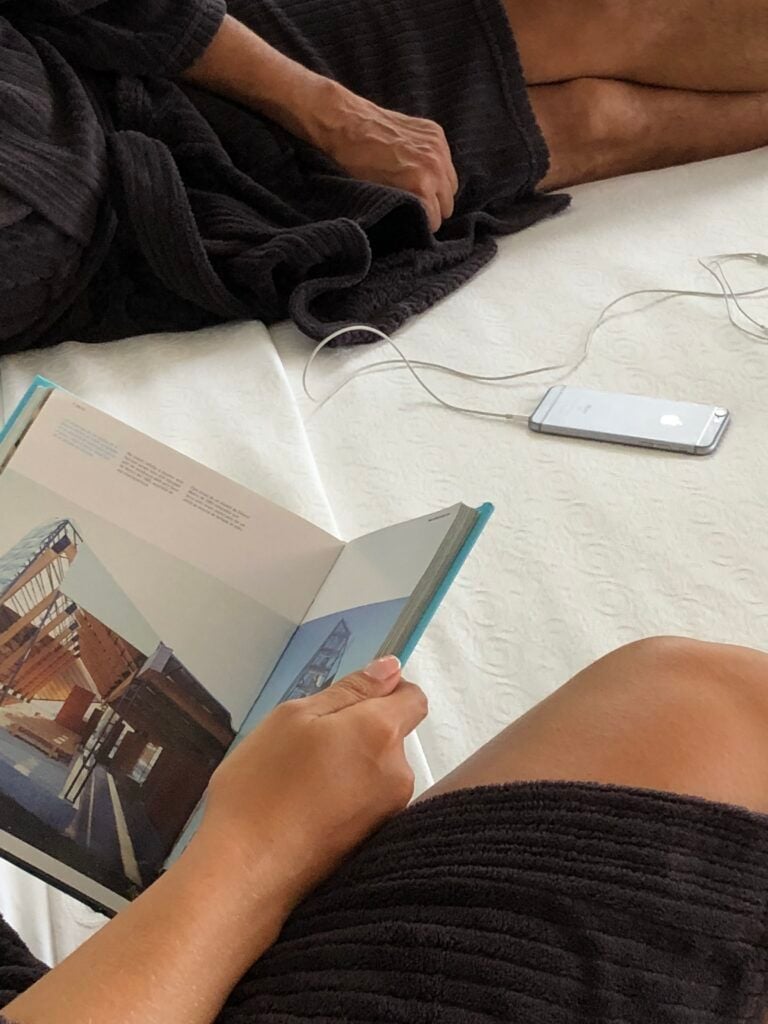 Casal em roupões pretos deitados na cama com livro e celular carregando