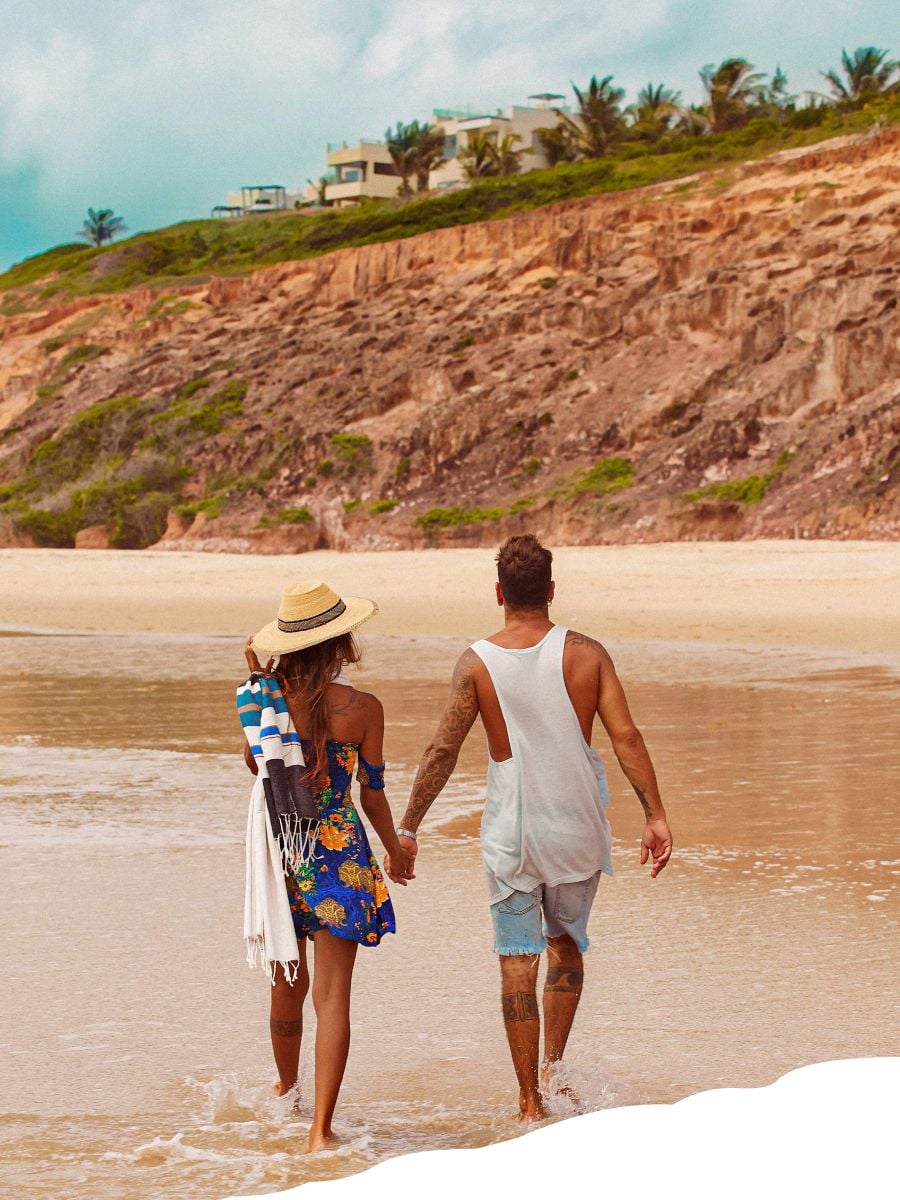 Casal de mãos dadas andando na paradisíaca praia de Sibaúma de frente ao hotel Kilombo Villas.