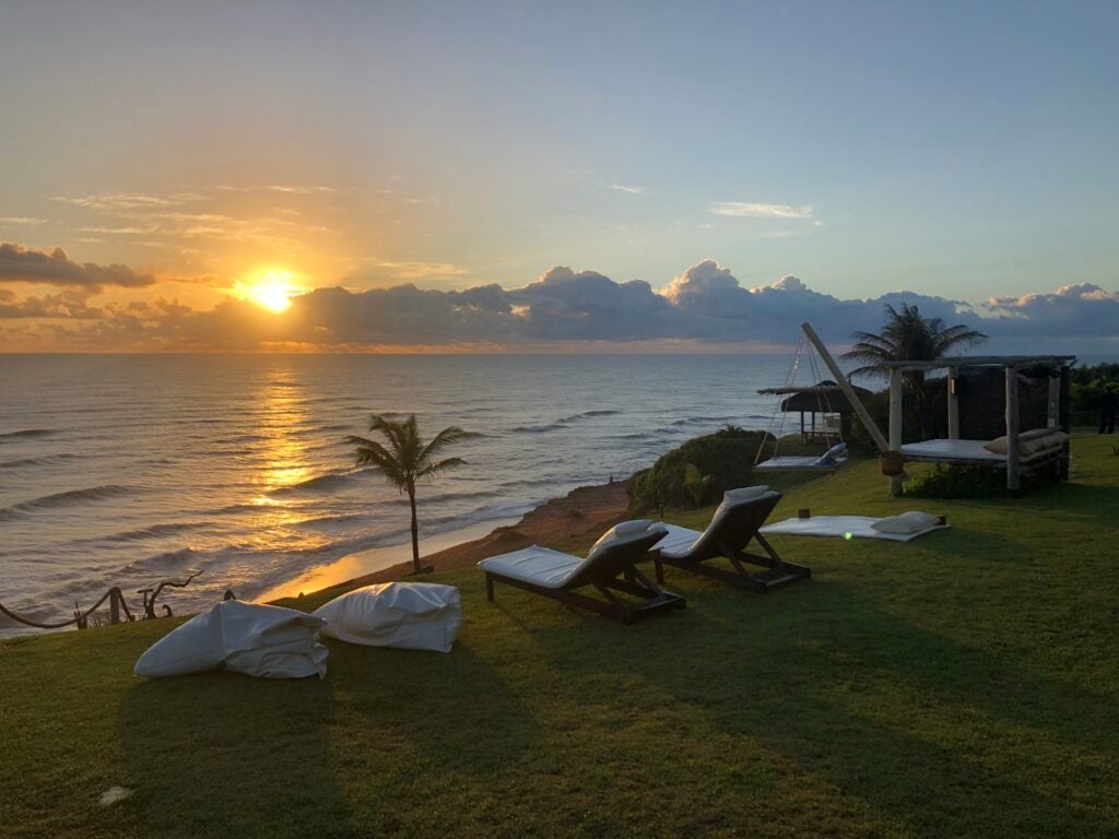 Pôr do sol dourado sobre o oceano com espreguiçadeiras e cama suspensa no jardim
