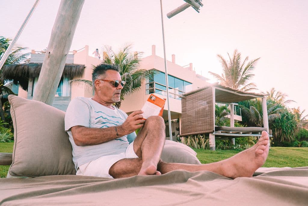 Hóspede lendo um livro em uma espreguiçadeira diante do Kilombo Villas, em meio a coqueiros