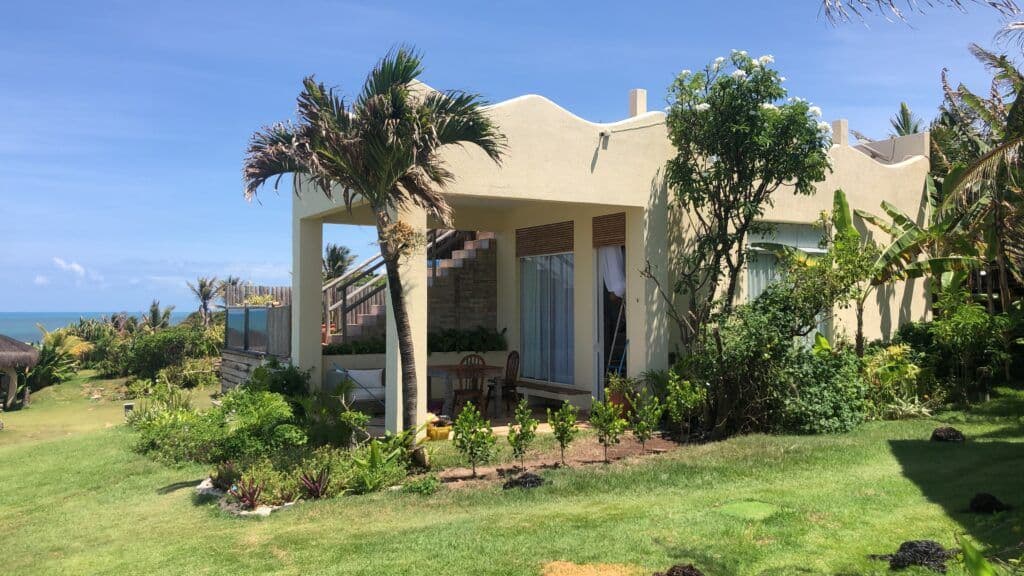 Villa rústica branca com jardim tropical exuberante, palmeira e piscina ao fundo