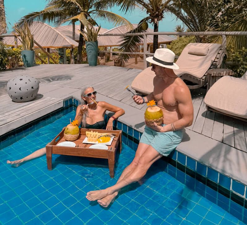 Casal aproveitando o day-use à beira da piscina com coco verde e frutas em bandeja