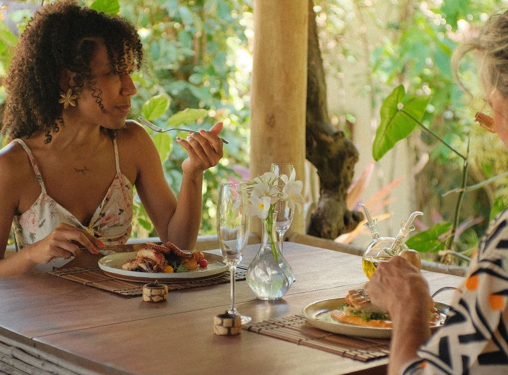 Casal almoçando em uma mesa de madeira cercada pela natureza no Kilombo Villas