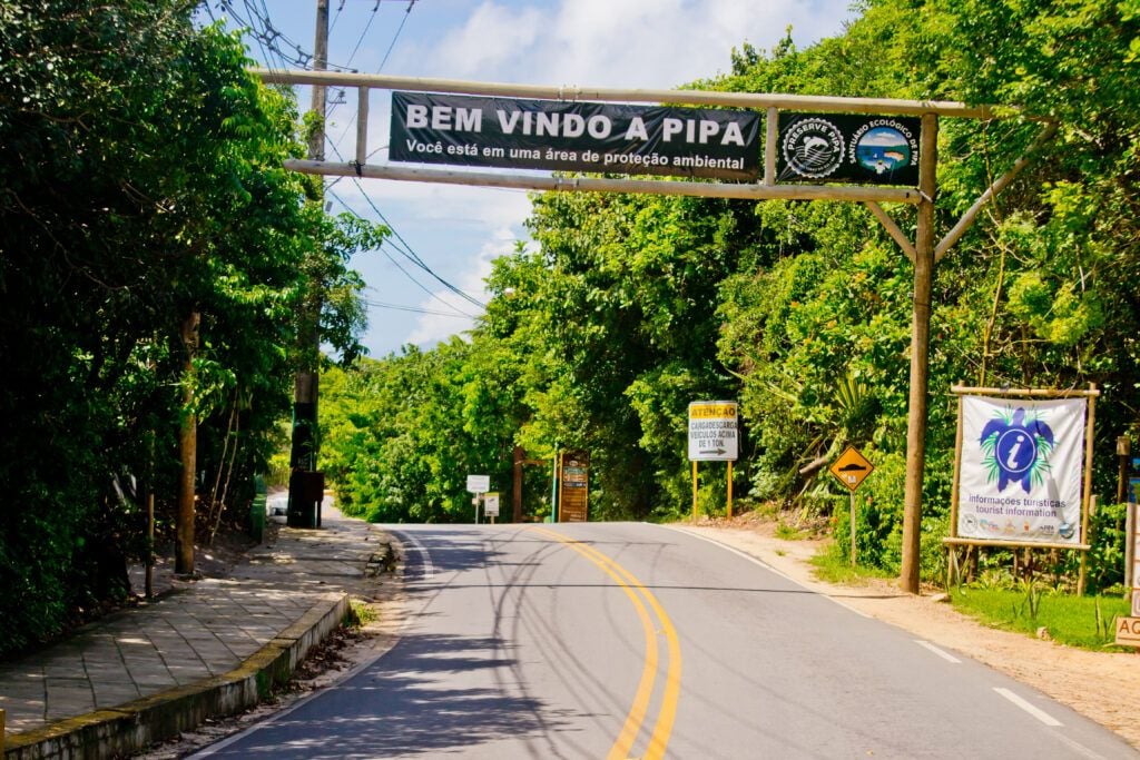 Placa "Bem Vindo a Pipa" na entrada da vila com vegetação tropical ao redor