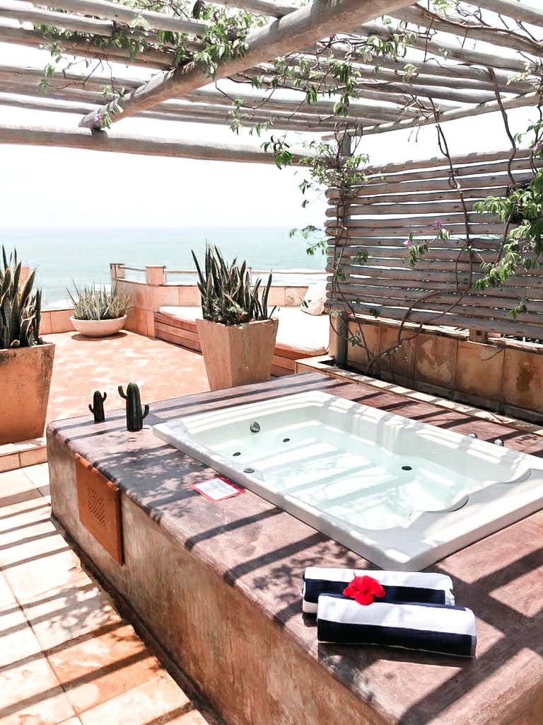 Villa branca com banheira de hidromassagem ao ar livre, cactos em vasos e vista para o mar